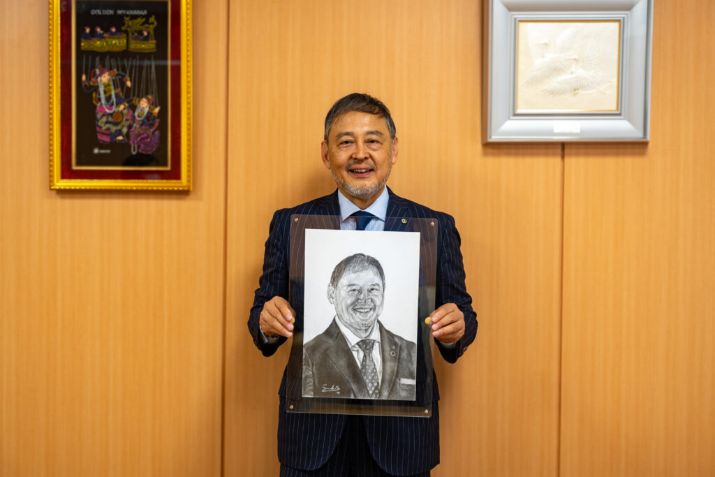 返礼としていただいた肖像画を持つ大橋聡司社長の写真